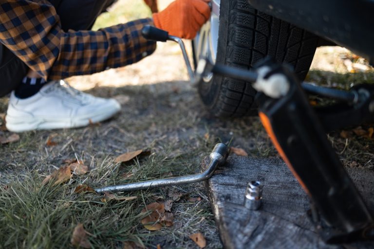 A close-up of a car jack and lug wrench used for a flat tire change.